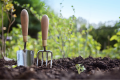 dirt with greenery in background and two tools sticking out of the dirt